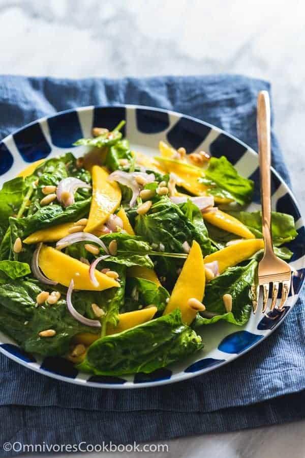Spinach mango salad in a black and white bowl with a fork