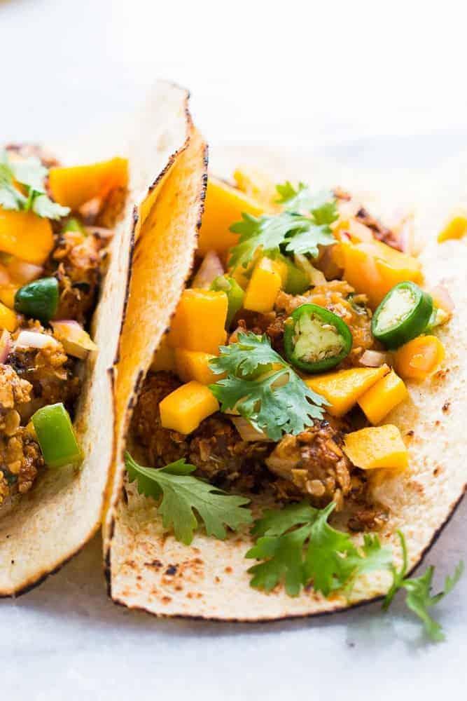 Two fish tacos with mango salsa on a marble countertop