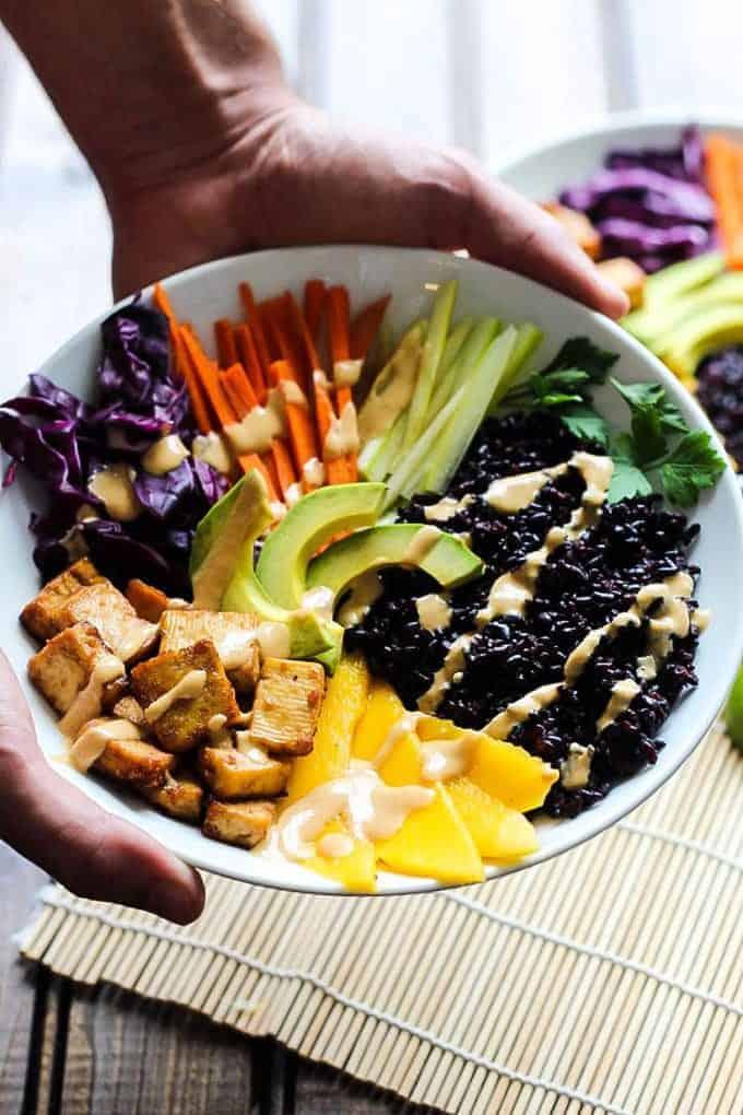 Tofu and forbidden rice bowls being held in a hand