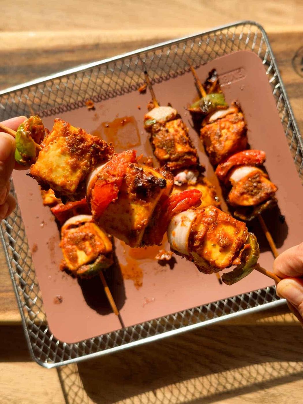a person holding a skewer of air fryer paneer tikka to showcase its color and texture