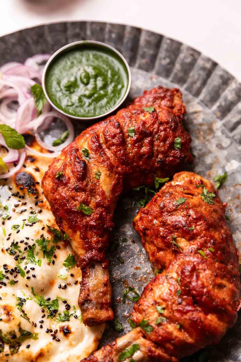 tandoori chicken served on a plate with naan, chutney, and sliced onions