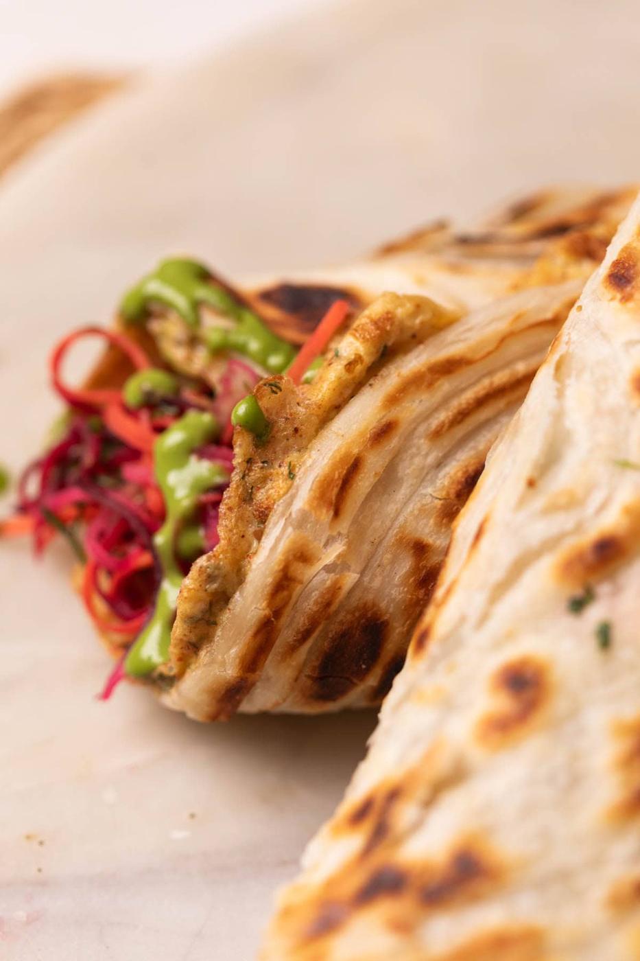close up image of rolled up anda paratha to show its flaky texture and filling