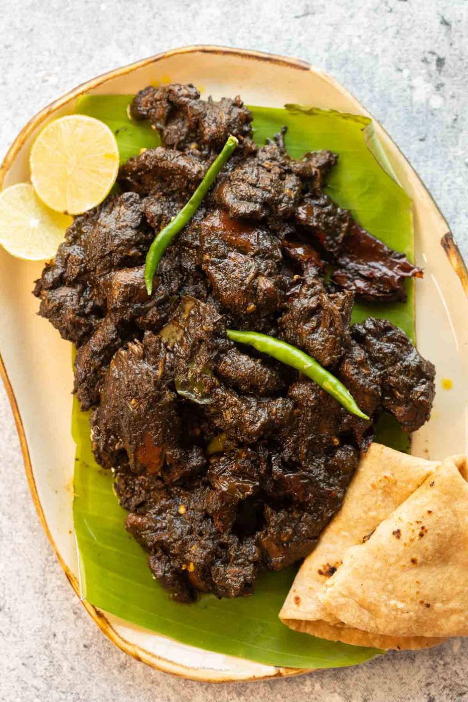 Black sesame chicken served on a platter with rotis and lime