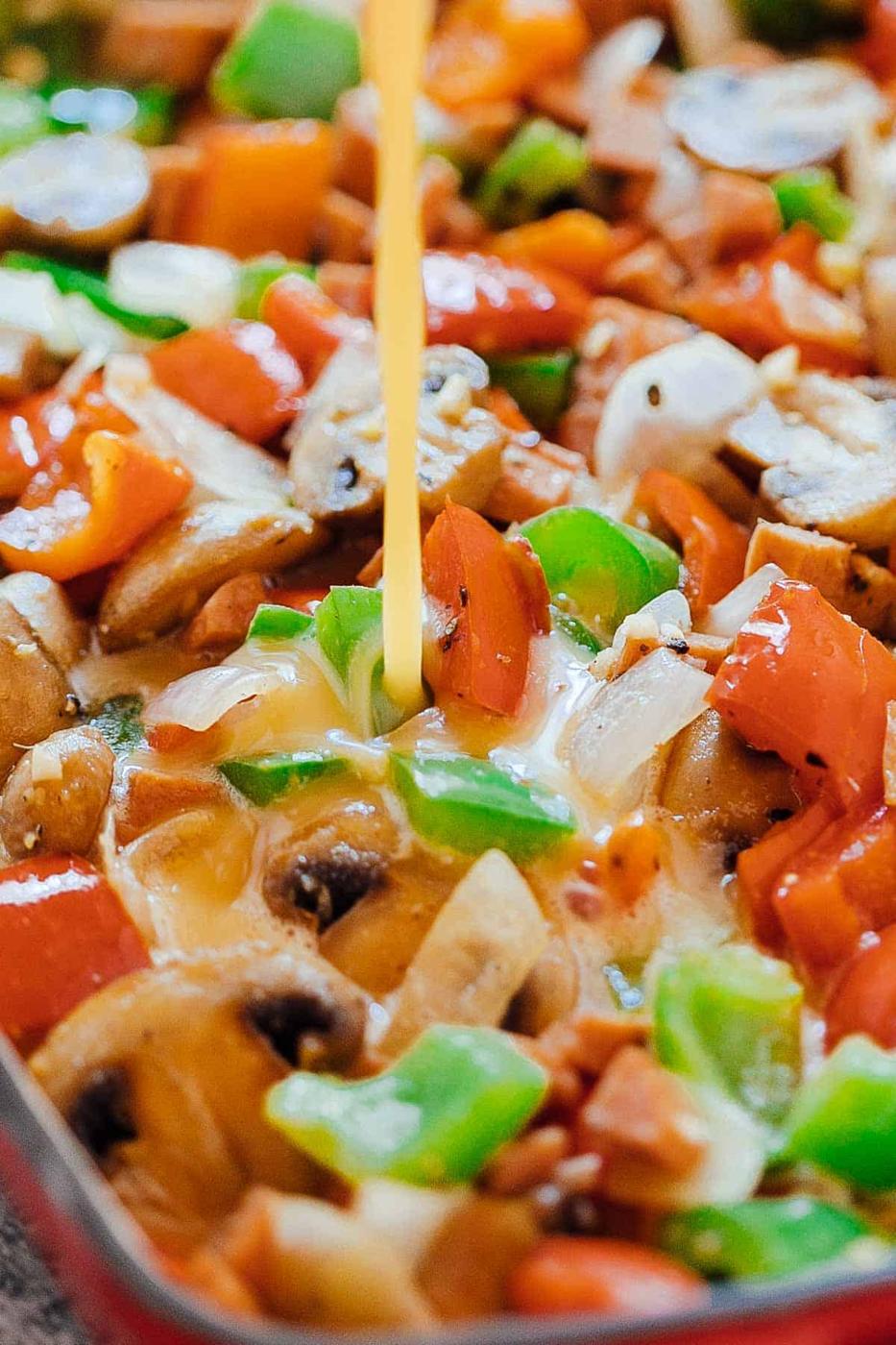 Pouring whisked egg over onions, peppers, mushrooms and ham for the baked denver omelet breakfast casserole