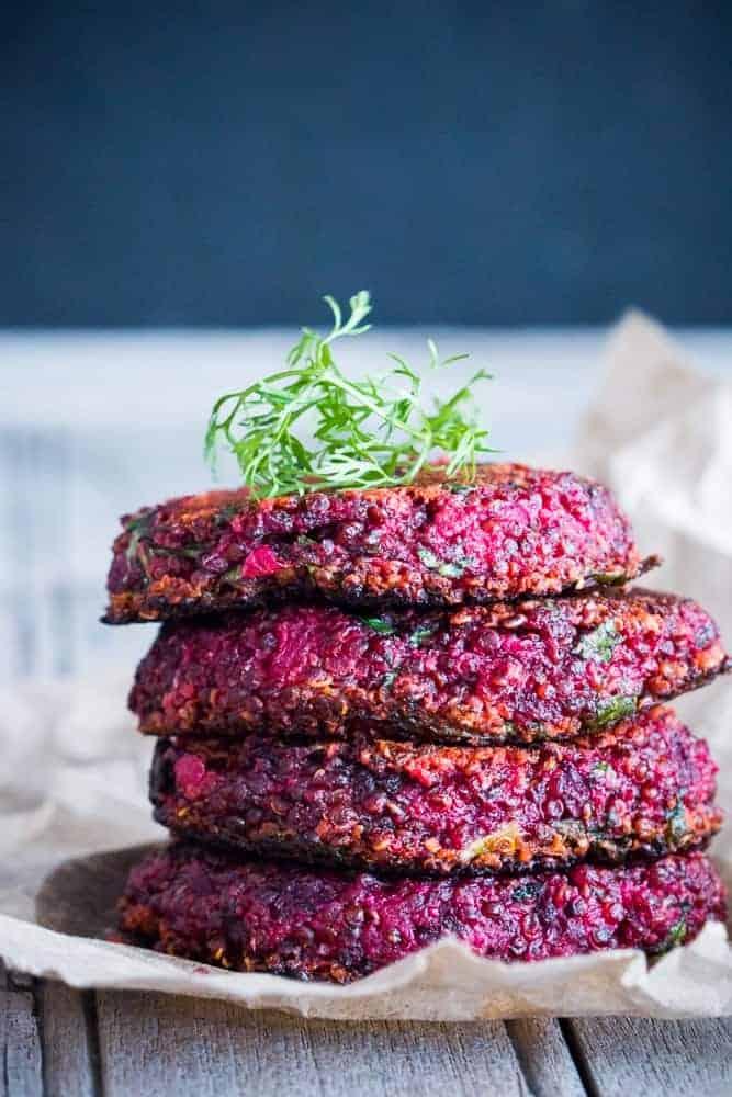 Four beet and goat cheese quinoa patties stacked one on top of another placed on crushed white paper