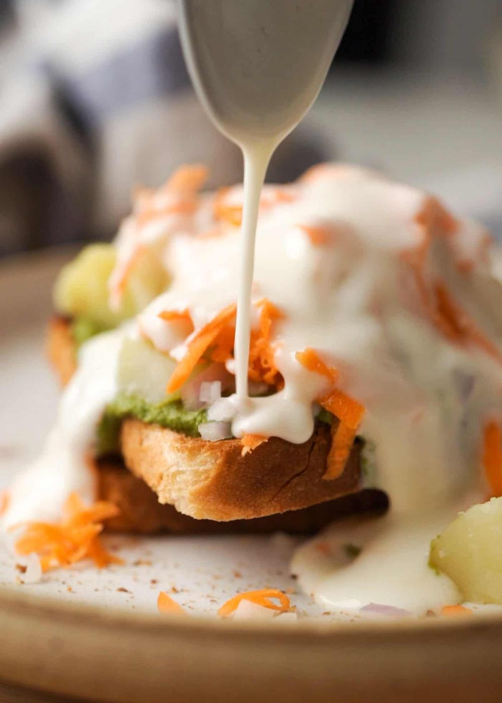 A picture of bread chaat being topped with curd