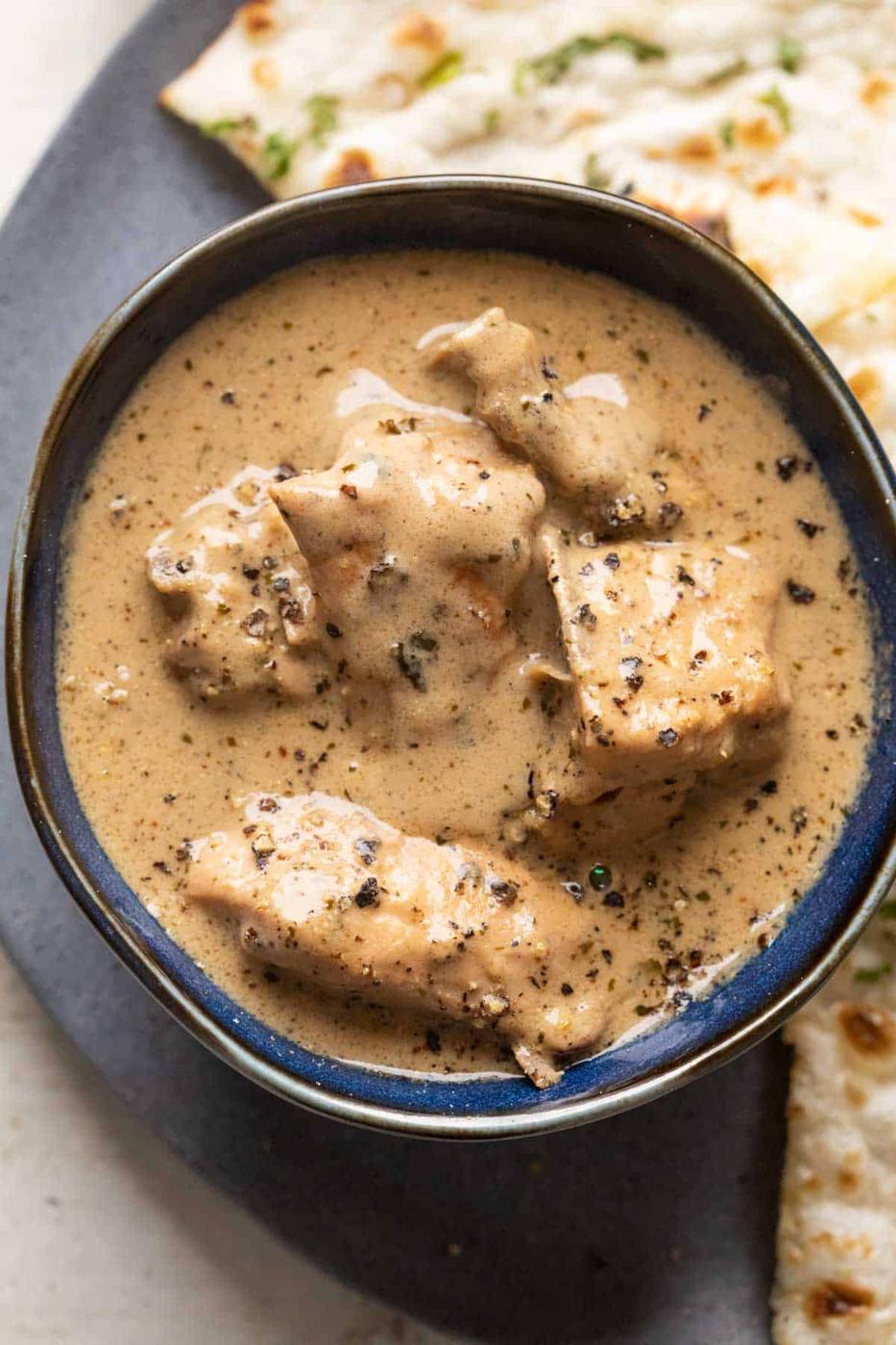 Chicken kali mirch gravy served in a blue bowl with naan on the side