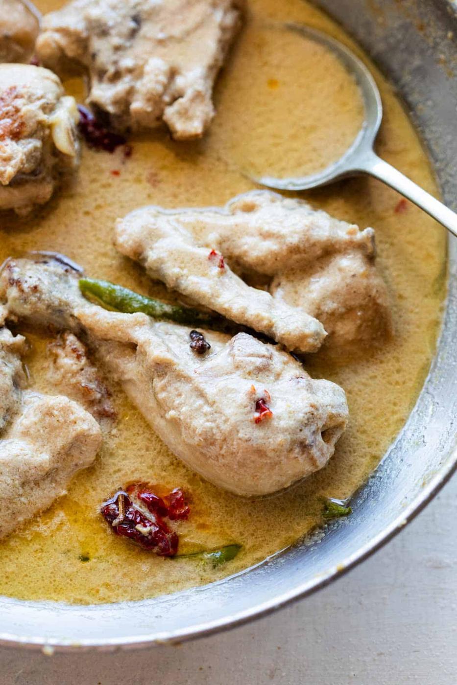 Cooked chicken rezala in an aluminium kadhai with a spoon
