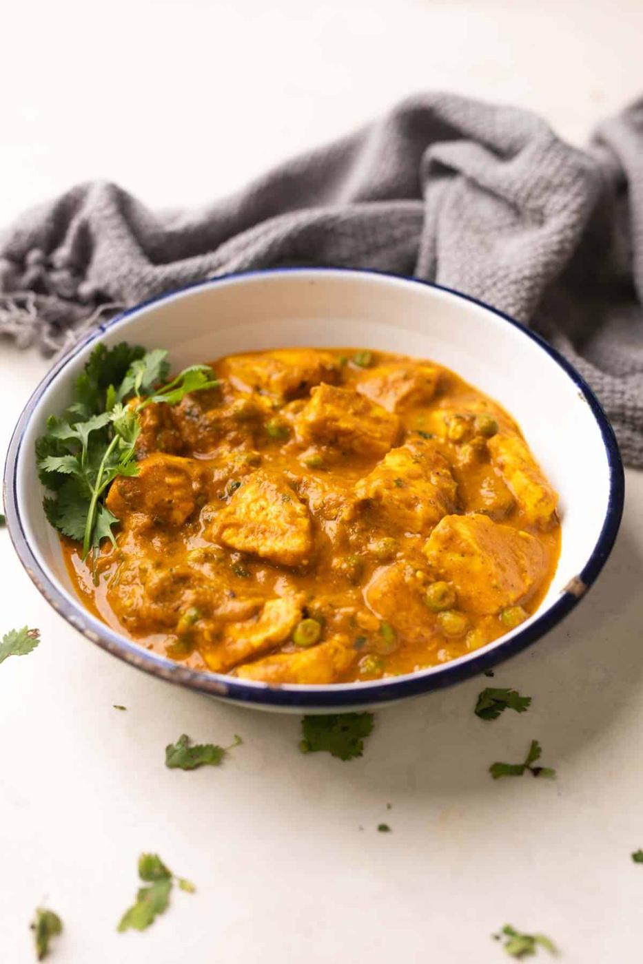 shot of matar paneer gravy in a white bowl with coriander sprinkled on top