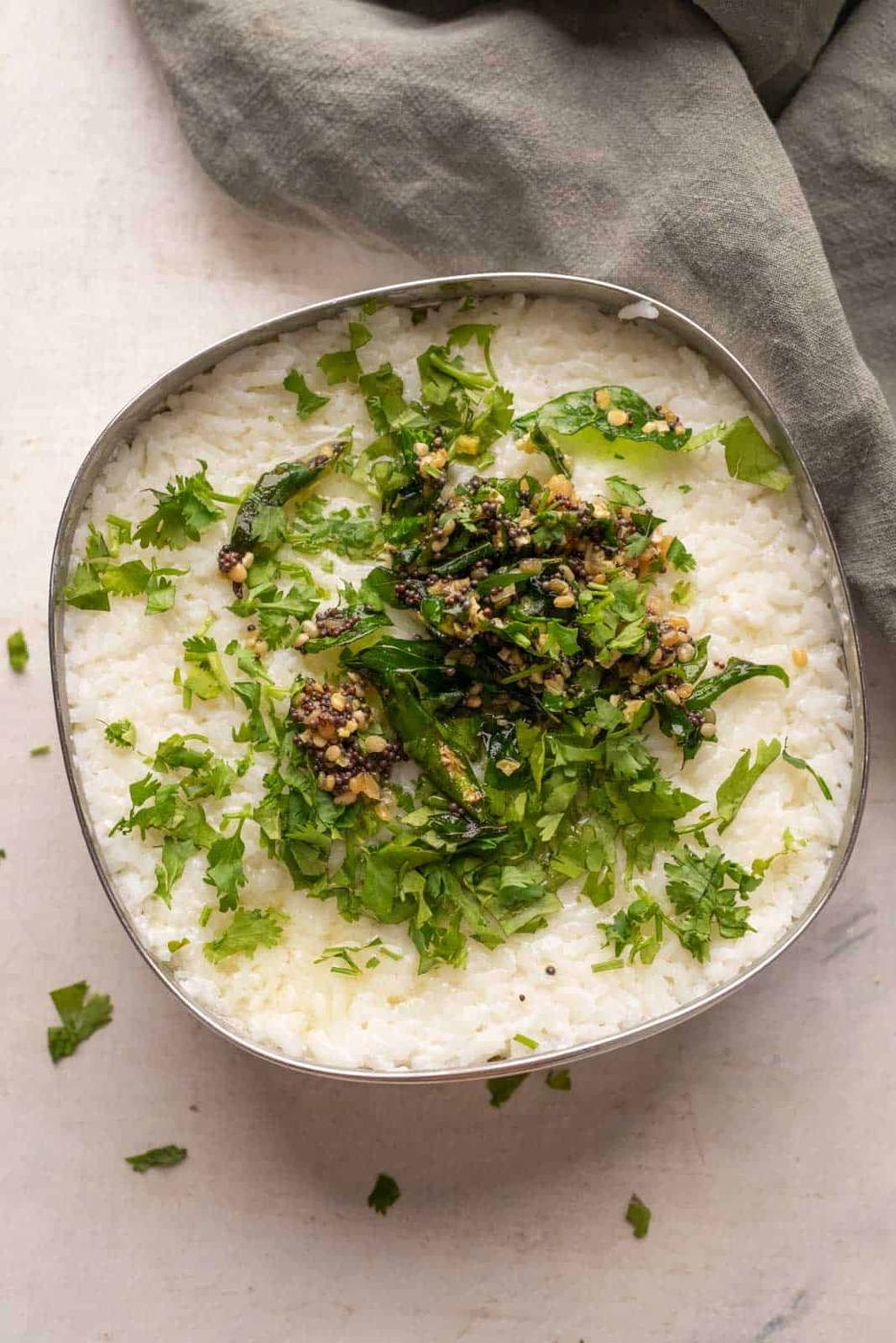 Curd rice set in a steel bowl topped with tempering and chopped coriander