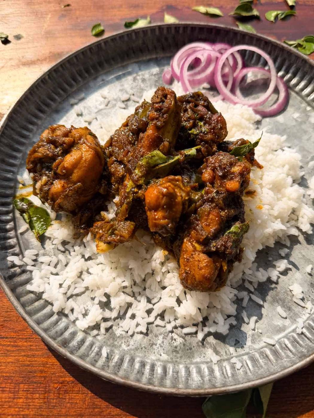 an image of curry leaf chicken served on a bed of rice with sliced onions on the side