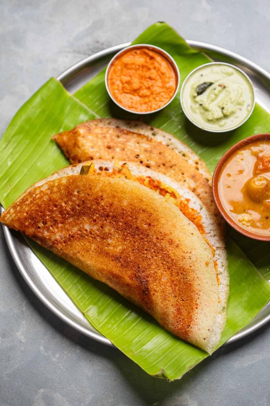 freshly made dosas served on a banana leaf platter with accompaniments