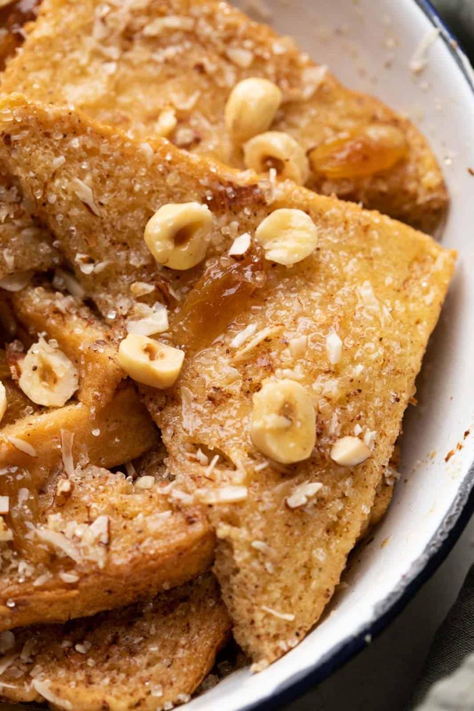 Closeup of a slice of bread from the bread pudding to show the beautiful texture thats glistening with melted butter and is topped with nuts and raisins