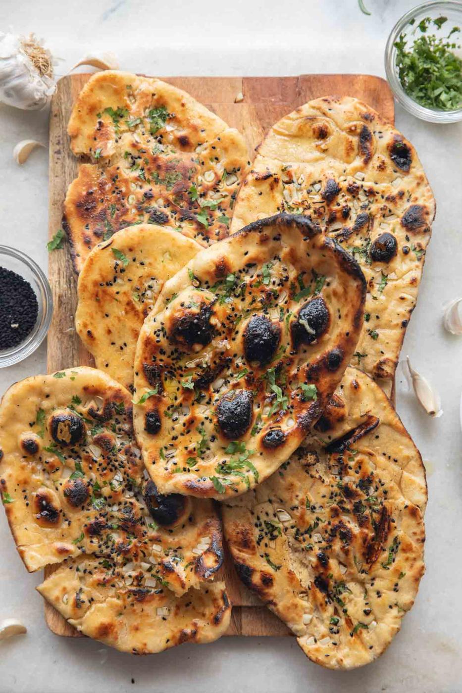 image of butter garlic naan stacked one on top of the other on a wooden board