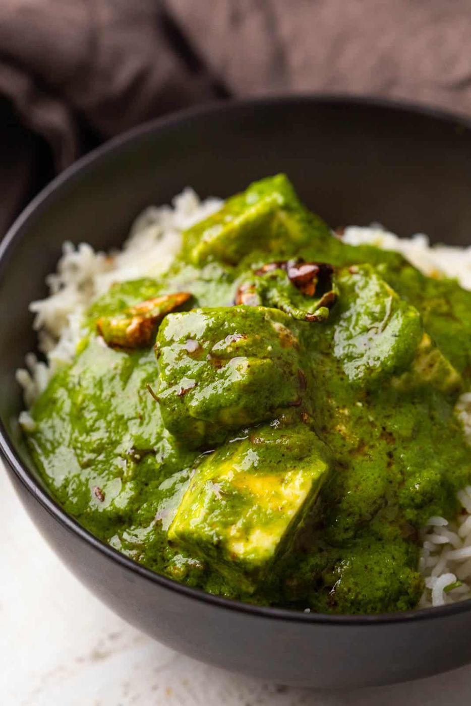 Palak paneer serve on top of jeera rice in a black bowl