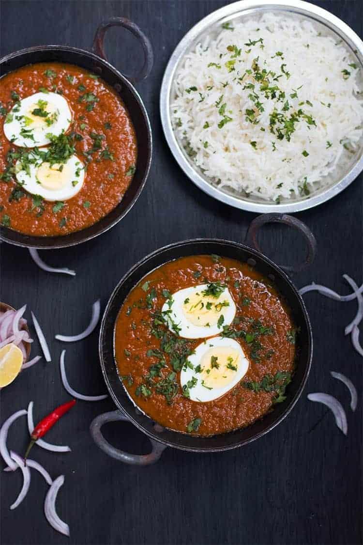 egg curry served in a small black kadhai with a plate of rice on the side