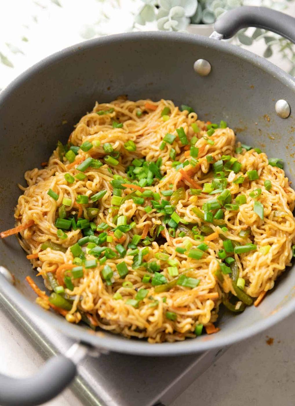 A shot of chinese maggi in a grey pan with spring onions