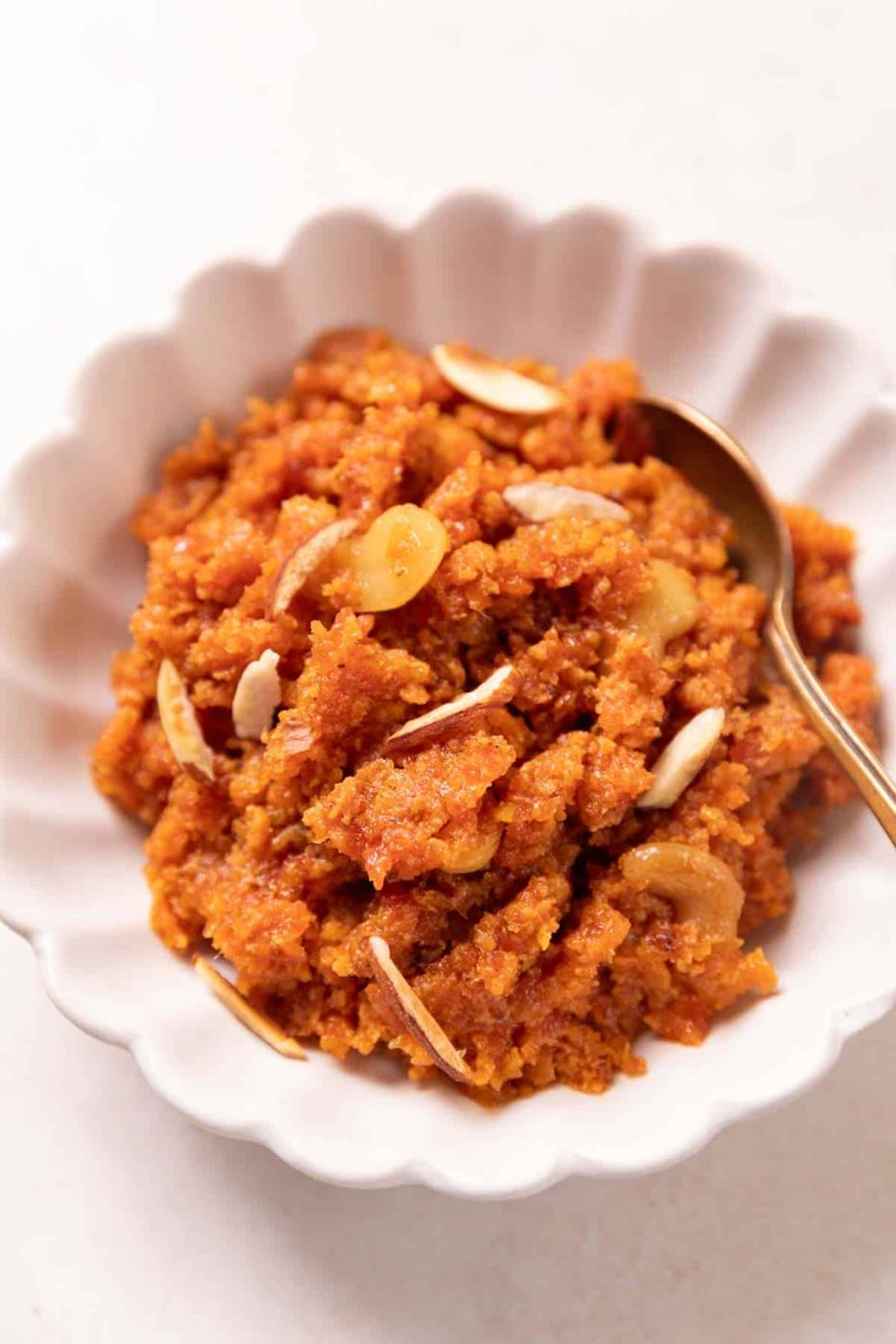 Gajar ka halwa served in a white bowl with almonds on top and a spoon on the side