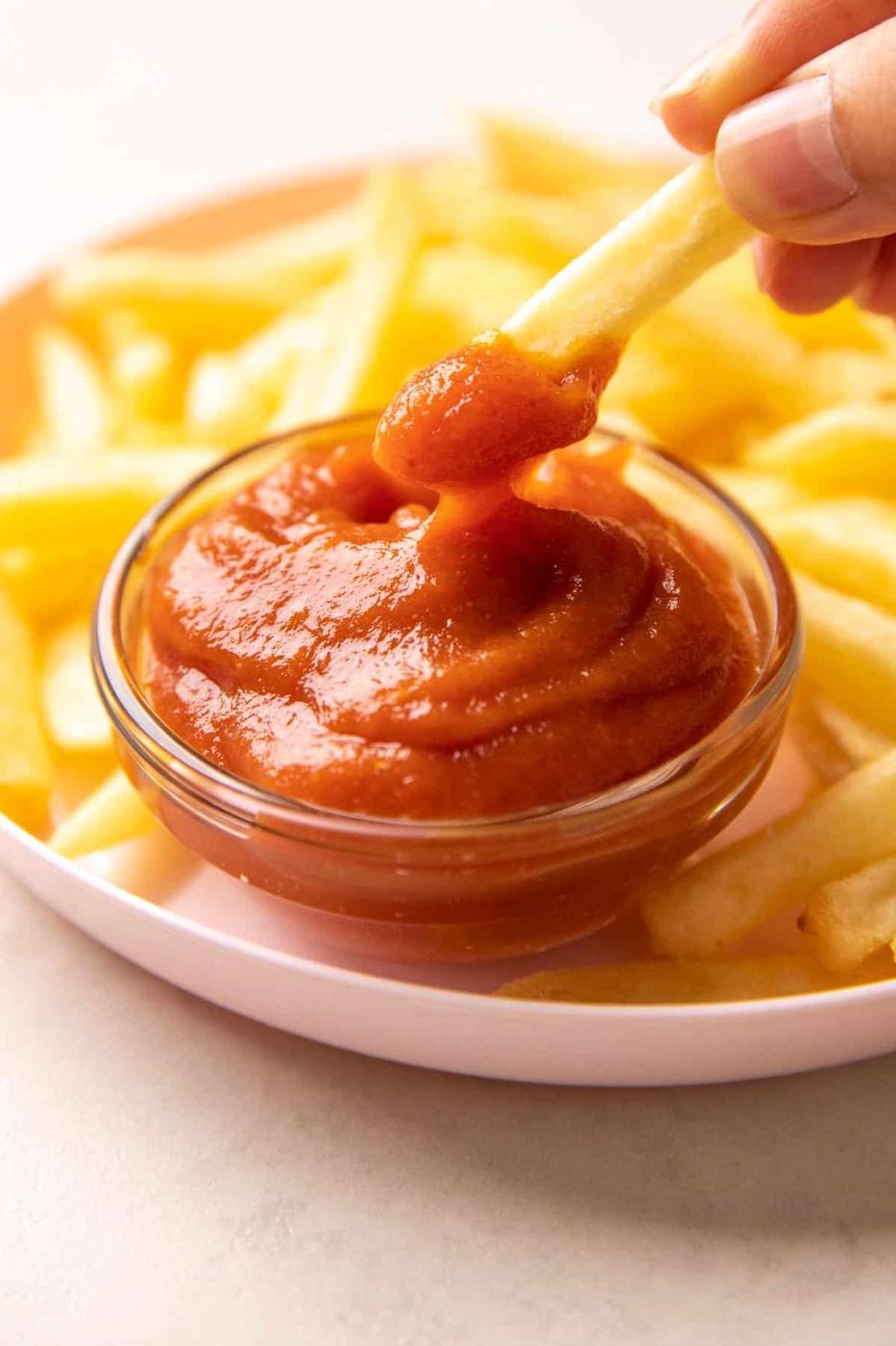 A french fry being dipped into a bowl of tomato ketchup