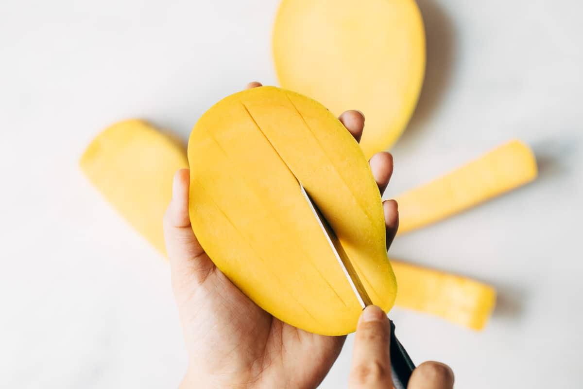 Vertical cuts being made on a mango to cut it into dices.