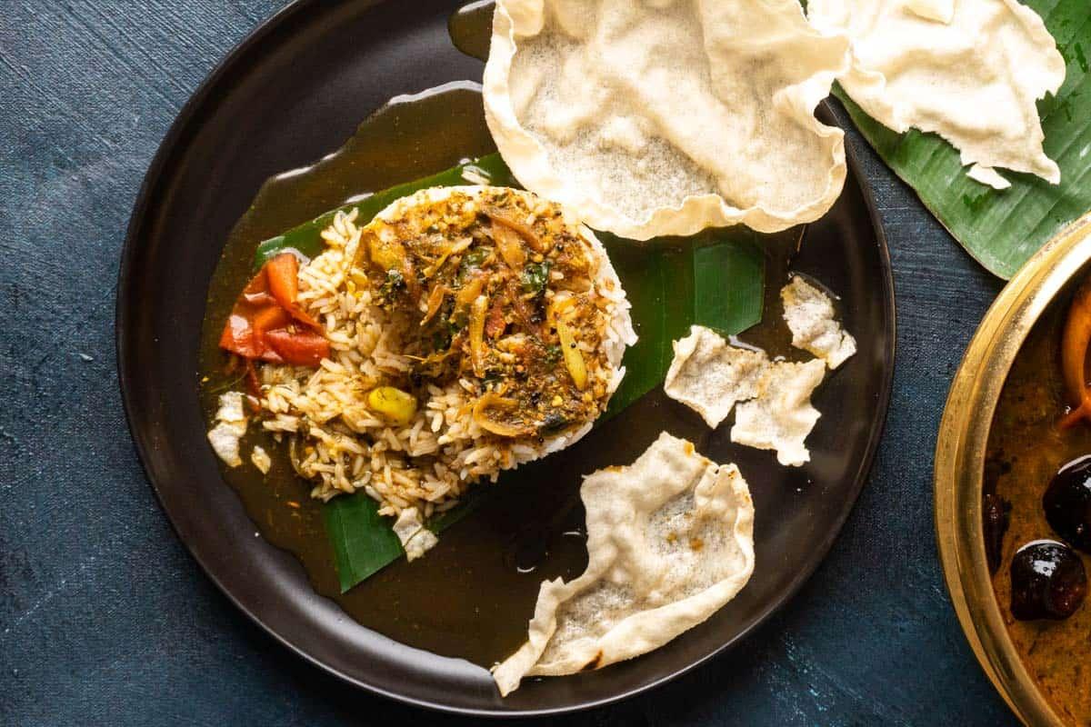 Picture of rasam poured over a mound of rice with papad on the side