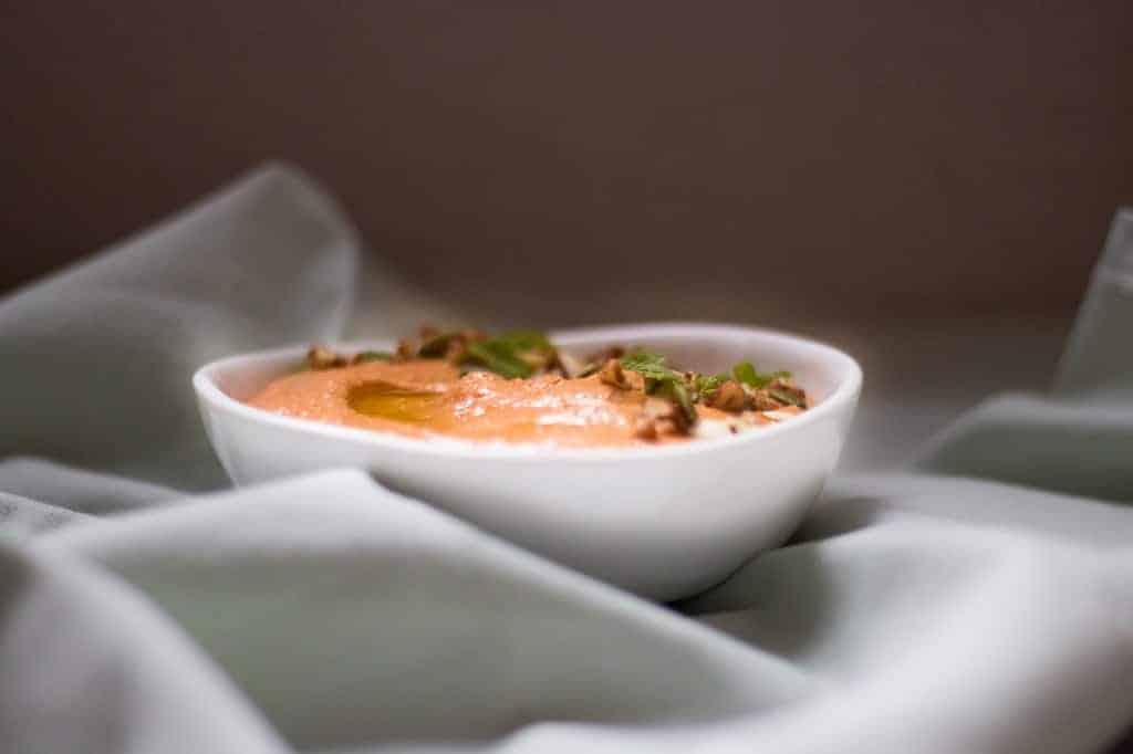 lebanese pecan red pepper dip garnished with pumpkin seeds served in a white bowl