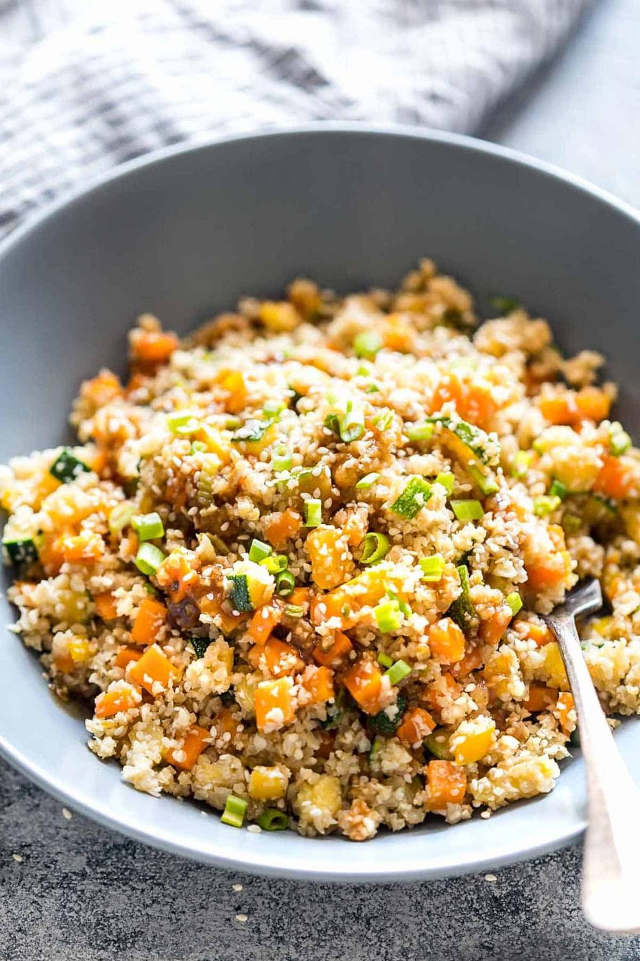 Low Carb Asian Cauliflower Rice topped with sesame seeds, chopped green onions and served in a bowl.