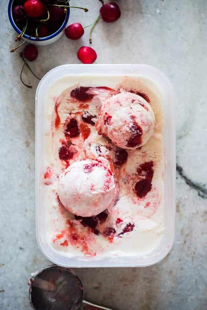 lychee cherry swirl icecream in a white tub with cherries on the side