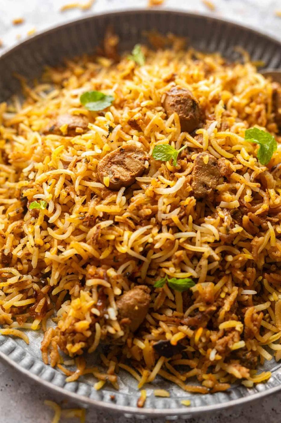 Close up of a dish of mushroom biryani to show the fluffy texture of rice, separate grains of rice and pieces of mushrooms dotted all around it