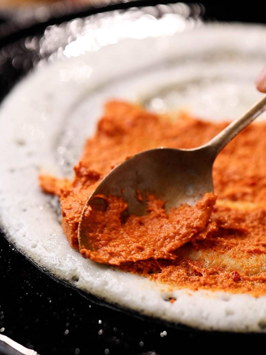 A spoon spreading chutney on dosa