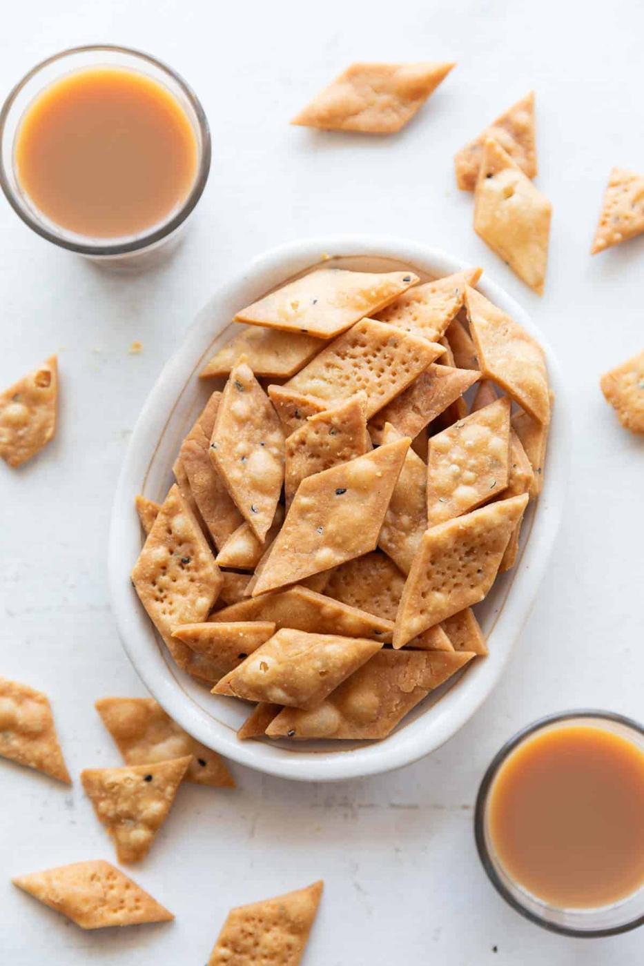 Picture of namak para in a white bowl with cups of chai around it