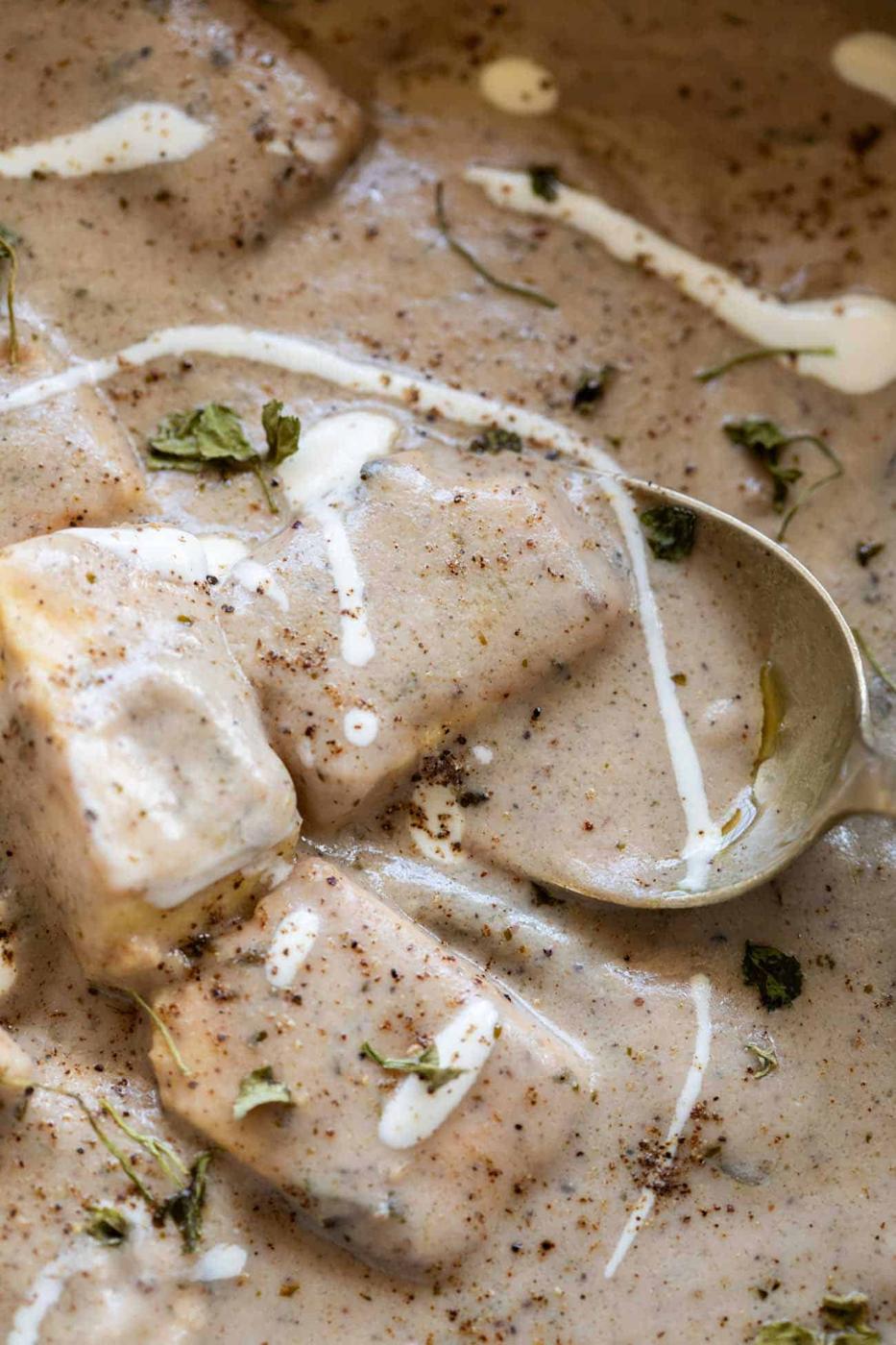 close up shot of paneer kali mirch gravy served in a bowl with cream drizzled on top