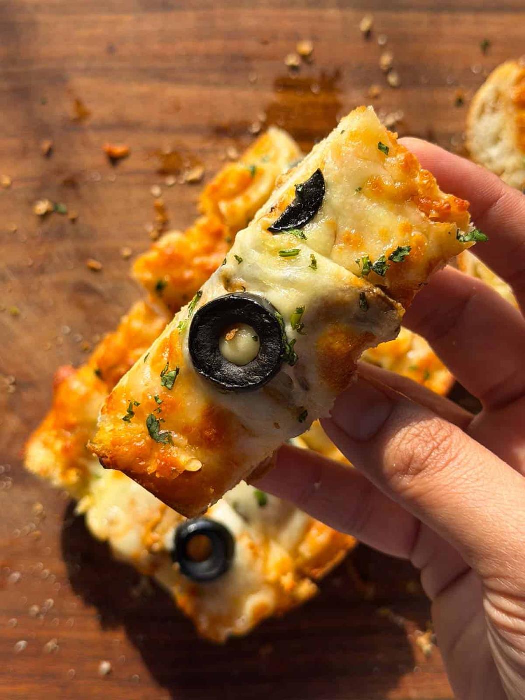 a person holding up a slice of the air fryer pizza garlic bread to showcase it's creamy and crispy texture