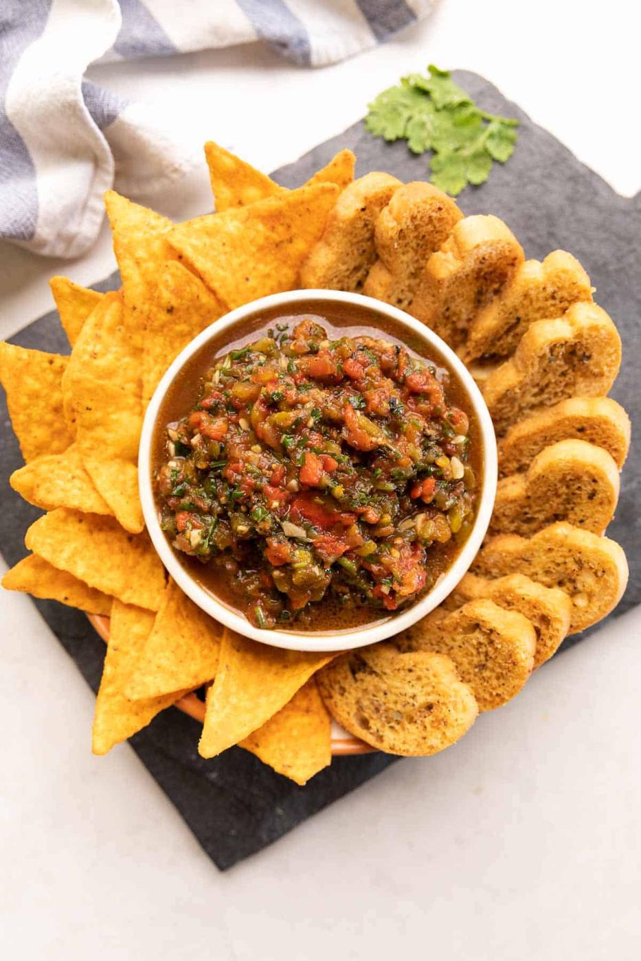 plate of nachos and crostini with a bowl of tomato salsa in the middle
