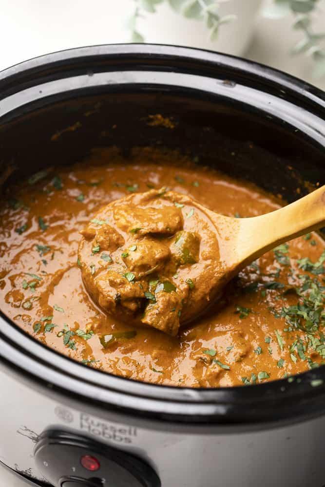 A shot of a ladle-full of chicken tikka masala in a slow cooker