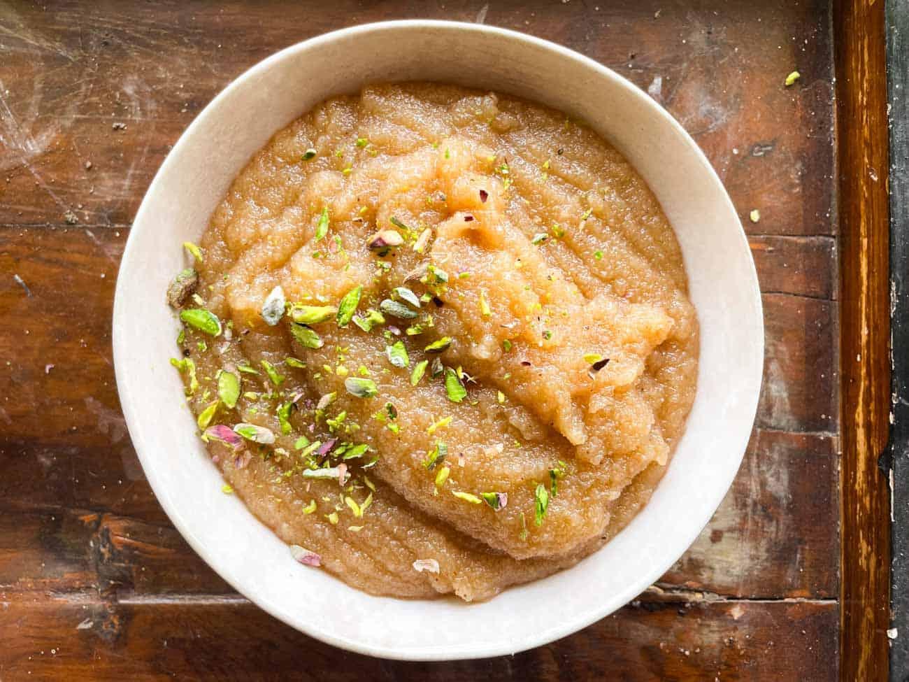 a white bowl with sooji halwa with sprinkled pistachio on top