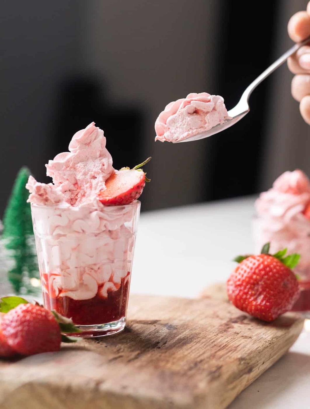 Strawberry mousse layered in a glass with strawberry compote topped with half a strawberry on a wooden board.