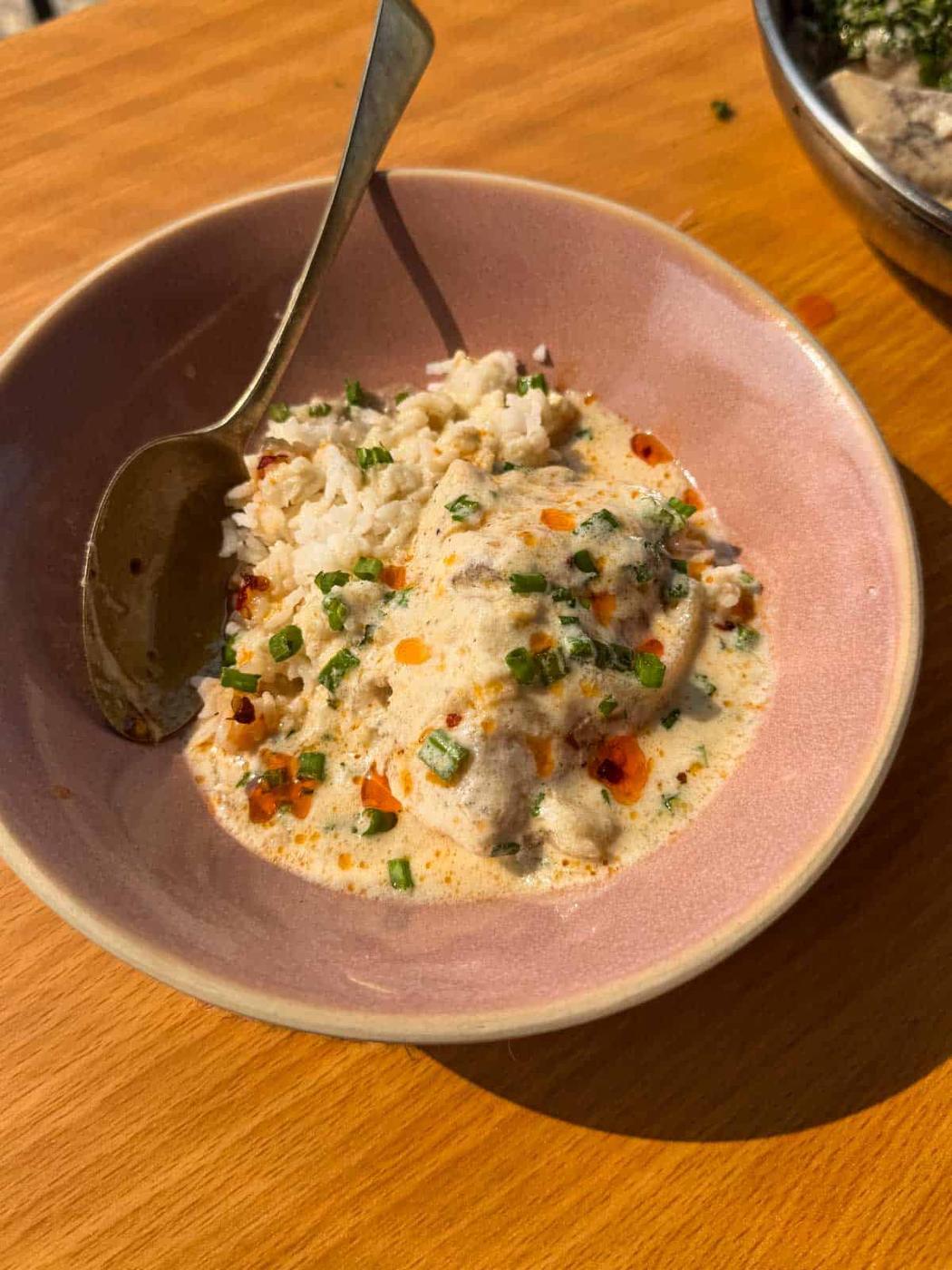 Picture of thai poached fish in coconut milk served on a bowl of rice with broth on the side