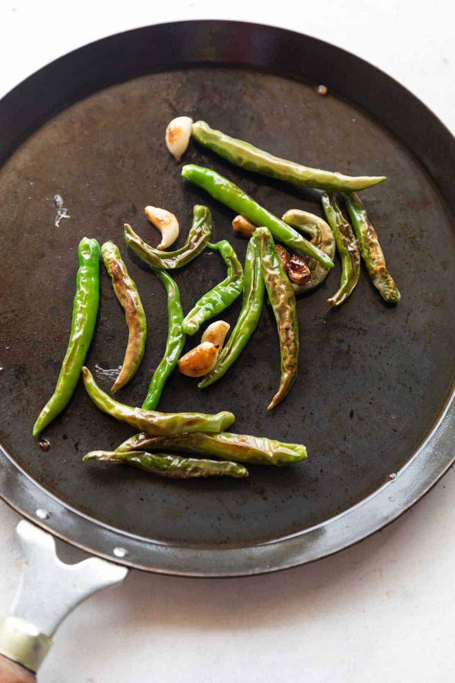 an image of blistered green chillies and garlic on a tawa to make thecha