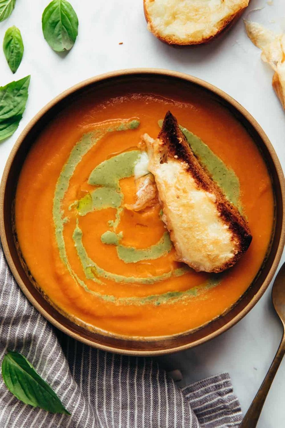 Roasted tomato pesto soup served in a bowl with toasted cheesy bread