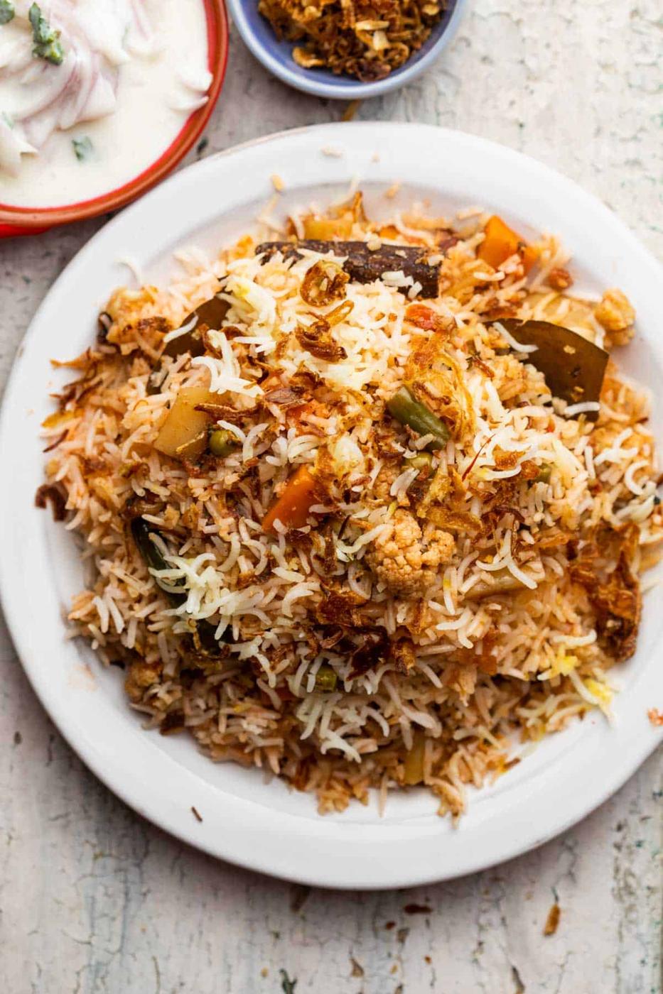 Veg Biryani served on a plate with raita and fried onions