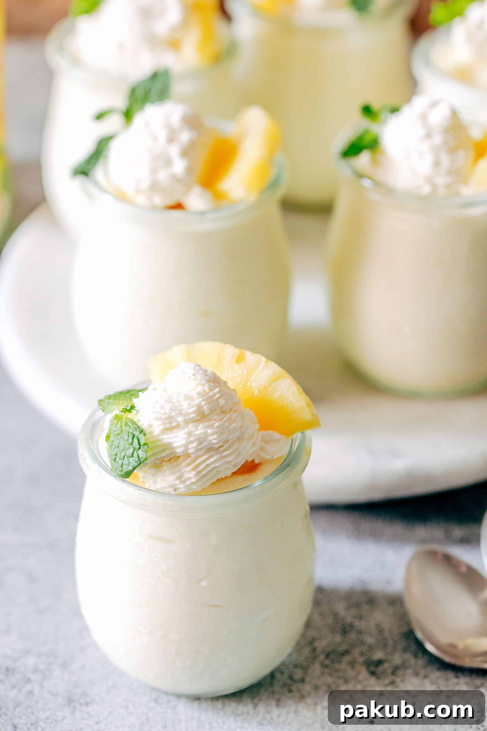 Tropical Escape: Eggless Pineapple Mousse 2 Creamy Eggless Pineapple Mousse cups garnished with fresh mint and pineapple chunks, served in elegant glass jars.