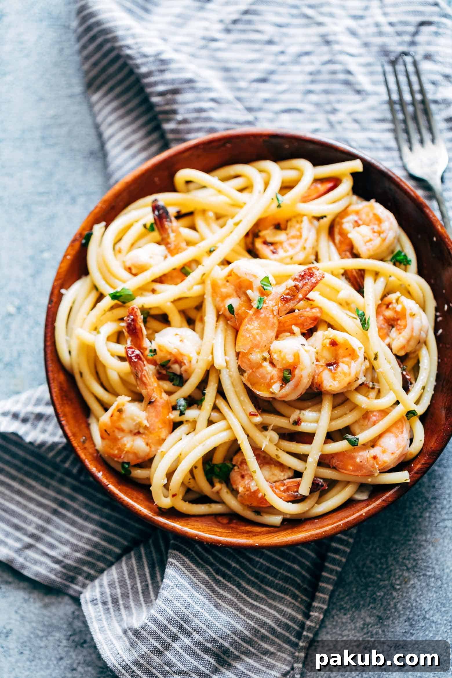 A close-up of the cooking process for Shrimp Spaghetti Aglio Olio, showing succulent shrimp being sautéed with garlic and chili flakes in olive oil, with pasta water beginning to form the sauce.