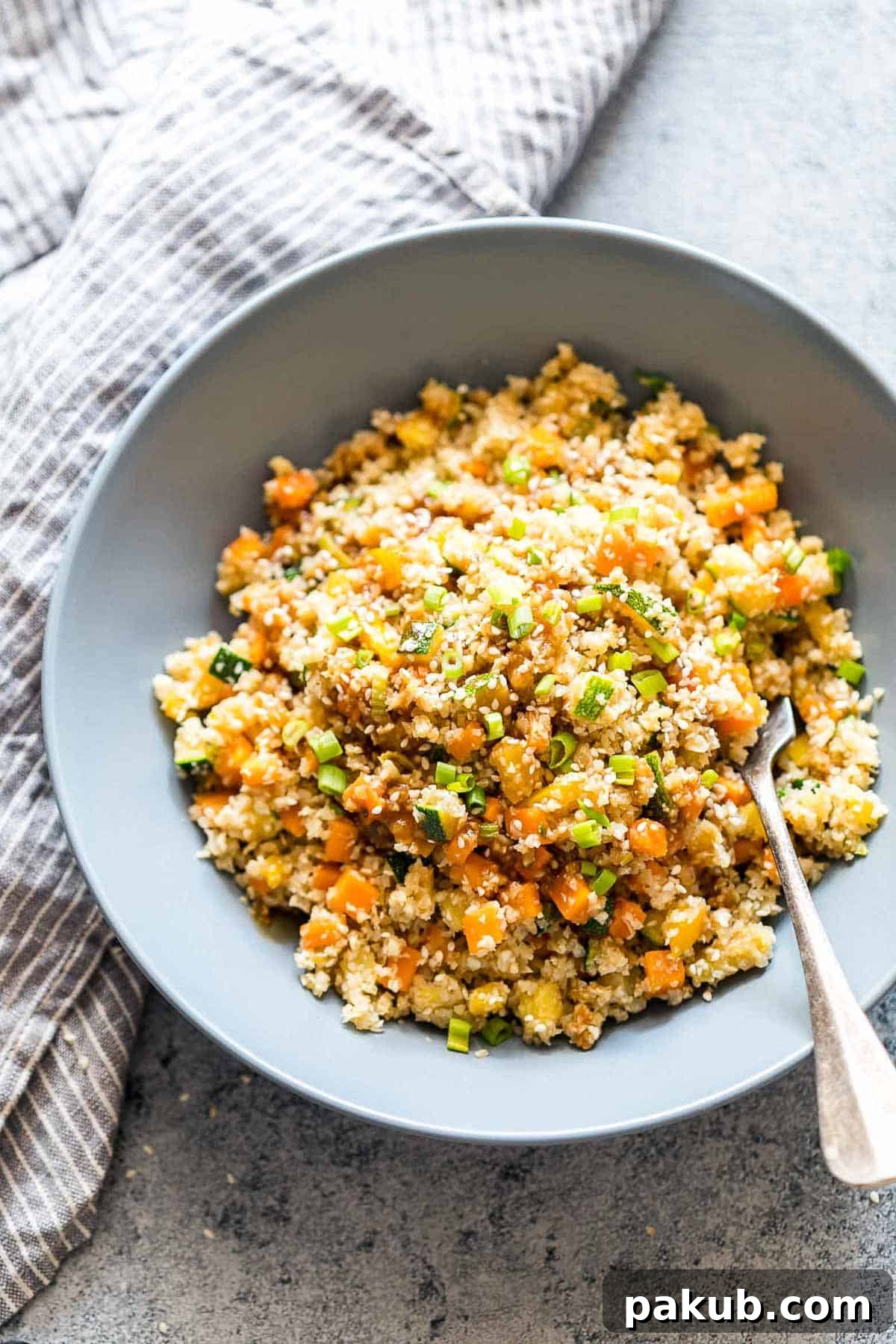 A beautifully presented bowl of Low Carb Asian Cauliflower Rice, garnished with toasted sesame seeds and chopped green onions.