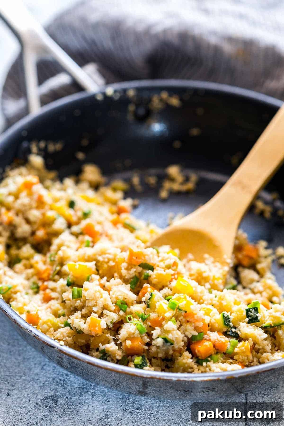 Low Carb Asian Cauliflower Rice being expertly tossed and stir-fried in a large pan with colorful vegetables, showcasing the cooking process.