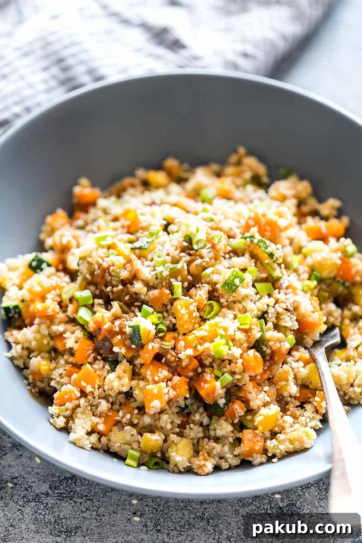Close-up shot of a bowl of Low Carb Asian Cauliflower Rice, beautifully topped with fresh green onions and sesame seeds, highlighting its fresh appeal.