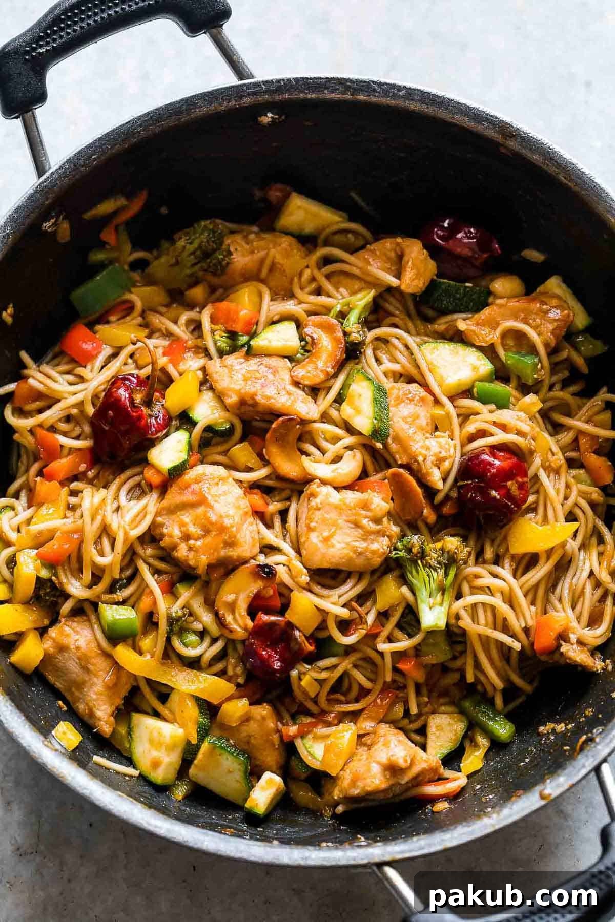 A vibrant pan of homemade Chinese Cashew Chicken Noodles Stir-Fry, showcasing golden-brown chicken, tender noodles, and colorful fresh vegetables like broccoli and bell peppers.