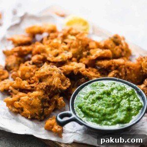 Crunchy vegetable pakoras served on a wooden board with fresh green coriander chutney