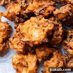 Closeup of crispy onion pakodas served on a board with accompanying dips