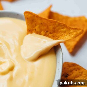 Nacho dipped in spicy nacho cheese sauce, highlighting its creamy texture